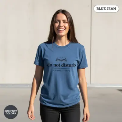 Comfort Colors garment-dyed t-shirt in Blue Jean featuring Do Not Disturb Currently Reading funny bookish typography graphic, worn in sunlight by female model