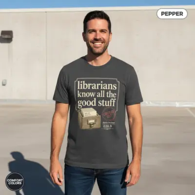 Pepper garment-dyed Comfort Colors tee printed with "Librarians Know All the Good Stuff" bold typographic phrase, worn outdoors in natural sunlight